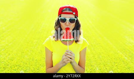 Sommerporträt einer glücklichen Frau, die Lutscher oder Eiscreme-Wassermelone auf dem Gras im Sommerpark isst Stockfoto