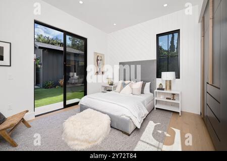 Ein modernes Schlafzimmer mit großem Fenster und Glasschiebetür, die in einen Garten führt. Stockfoto