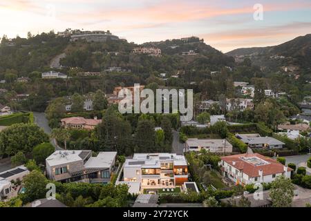 Blick aus der Vogelperspektive auf ein luxuriöses Wohnviertel in einer hügeligen Gegend bei Sonnenuntergang mit modernen und klassischen Häusern umgeben von üppigem Grün. Stockfoto