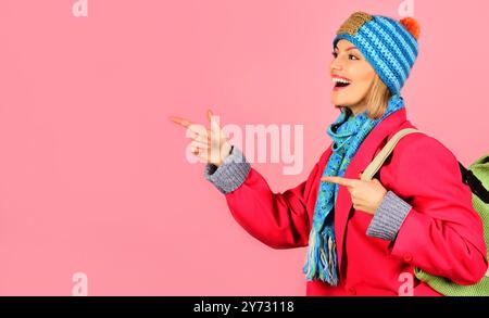 Lächelnde Frau in blauem Hut, Schal und rotem Mantel mit Handtasche, die mit den Fingern auf den Kopierraum für Werbung zeigt. Saisonangebot und Rabatt. Stilvolles Mädchen in f Stockfoto