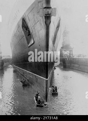 Die Königin Elizabeth im Trockendock. Nach 12 Stunden wegen ungünstigen Wetters zieht die Queen Elizabeth heute, Mittwoch, von der Geburt 101 in Southampton, New Dock, ins King George V Trockendock, um die nächste Stufe ihres Umbaus vom Truppenschiff zum luxuriösen Passagierschiff zu machen. Die Operation, das riesige Liner ins Dock zu bringen, wo sie etwa zwei Wochen frei bleiben wird, dauerte fast 90 Minuten. Am 16. Oktober soll sie ihre Jungfernfahrt von Southampton nach New York als Passagierschiff antreten. Foto zeigt, dass Hafenarbeiter mit der Reinigung des riesigen Rumpfes der 85.000 Tonnen schweren Queen Elizabeth beschäftigt sind Stockfoto