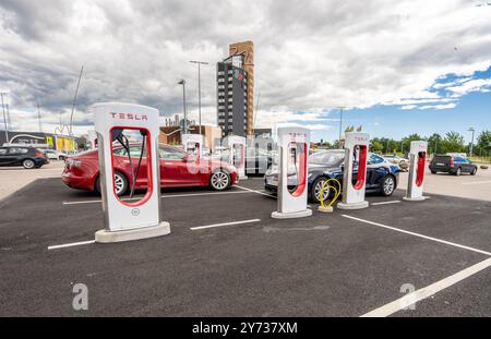 Halmstad, Schweden - 10. Juli 2022: Lange Reihe von Tesla-Autos laden am Tesla Supercharger Halmstad auf. Stockfoto