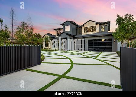 Modernes zweistöckiges Haus mit einer wunderschön gestalteten Auffahrt und üppigem Grün bei Sonnenuntergang. Stockfoto