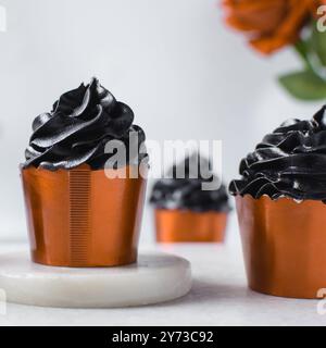 Orange Cupcakes mit schwarzem Buttercremewirl, Cupcakes in orangefarbenen Folieneinlagen mit schwarzer Buttercreme, Frosted Halloween Cupcakes auf weißem Hintergrund Stockfoto