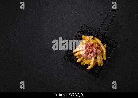 Knusprige Pommes frites mit Speckstücken, Salz und Gewürzen auf dunklem Betonhintergrund Stockfoto