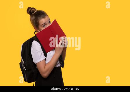 Ein Schulmädchen versteckt ihr Gesicht hinter einem roten Buch. Stockfoto