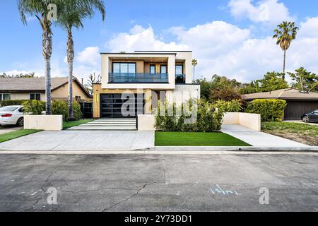 Modernes zweistöckiges Haus mit großen Fenstern, Palmen und einer sauberen Auffahrt unter einem hellblauen Himmel. Stockfoto