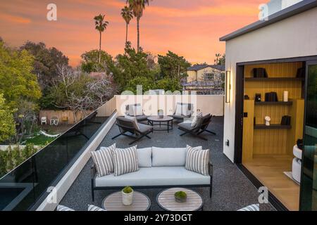 Moderne Dachterrasse mit stilvollen Gartenmöbeln und Blick auf den Sonnenuntergang, üppiges Grün und gemütlicher Sitzecke. Stockfoto