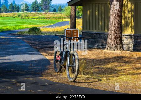 SCHWARZES MOUNTAINBIKE, DAS SICH AUF EINEM RICHTUNGSSCHILD AUF EINEM REITWEG IN SUNRIVER OREGON IN DER NÄHE EINES GEBÄUDES AN EINEM OFFENEN FELD LEHNT Stockfoto