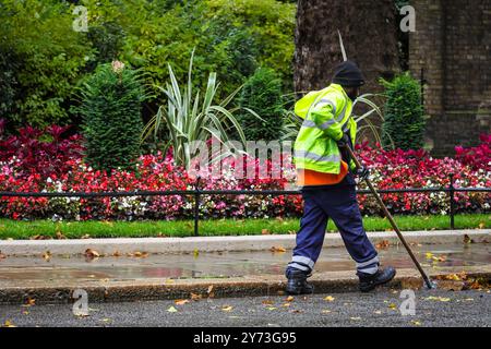 London, Großbritannien. September 2024. Ein Mitarbeiter des Westminster council fegt fleißig die Straße und den Straßenbelag in der Downing Street und sammelt Haufen von bunten, gefallenen Blättern. An einem dezidiert herbstlichen Tag im Zentrum Londons wurden heute starke Schauerwellen, Blauwind und kältere Temperaturen beobachtet. Quelle: Imageplotter/Alamy Live News Stockfoto