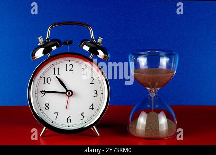Sanduhr und traditioneller Wecker, Nahansicht auf roter Basis und blauem Hintergrund Stockfoto