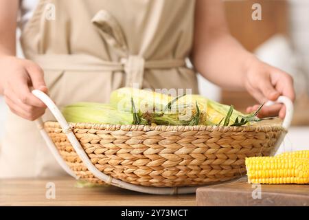 Frau, die Korbkorb mit frischen Maiskolben auf Holztisch hält Stockfoto