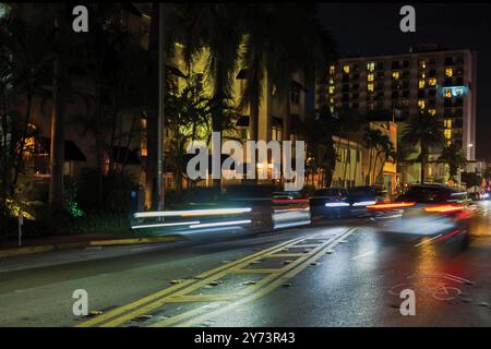 Nachtansicht auf Lichtwege von vorbeifahrenden Autos auf der Collins Avenue in Miami Beach mit Palmen und Gebäuden im Hintergrund. Stockfoto