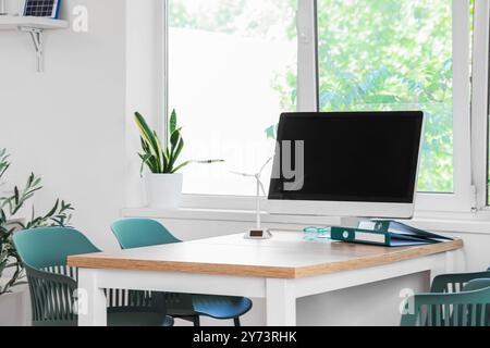 Computer mit Windkraftanlagenmodell und Mappen auf dem Tisch im Büro des Ingenieurs Stockfoto