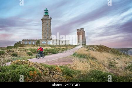 Eine nette Seniorin radelt mit ihrem E-Mountainbike an der felsigen smaragdgrünen Küste der Bretagne neben Cap Frehel Stockfoto