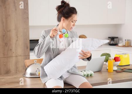 Überwältigte asiatische Mutter im Anzug mit Baby, Schnuller und Spielzeug zu Hause. Multitasking-Konzept Stockfoto