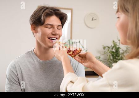 Eine junge Frau, die ihren Freund mit leckerer Pizza im Wohnzimmer füttert Stockfoto