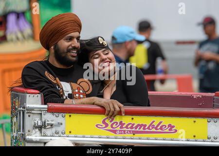 Saint John, NB, Kanada - 22. Juni 2024: Ein Paar reitet auf einer lokalen Messe auf dem Scrambler. Der Mann trägt einen Turban. Beide Leute lächeln. Stockfoto