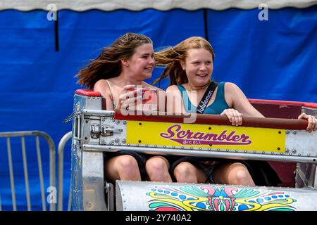 Saint John, NB, Kanada - 22. Juni 2024: Zwei Mädchen reiten auf dem Scrambler auf der lokalen Messe. Man hält ein Handy, als würde man ein Selfie machen. Stockfoto