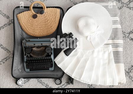 Offener Koffer mit Vintage-Schreibmaschine und Kleidung auf Teppich, Blick von oben Stockfoto