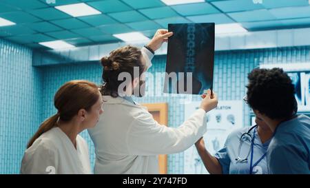 Das Klinikteam untersucht Röntgenstrahlen und diskutiert die Behandlungsstrategie in einem medizinischen Schrank. Arzte mit Expertise in Radiologie und Krankheitsprävention, die kollektive Arbeit für den Gesundheitsdienst leisten. Kamera A.. Stockfoto