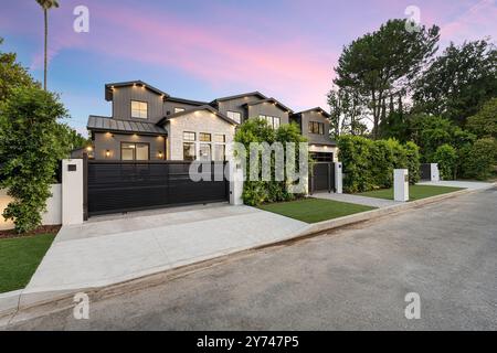 Modernes Luxushaus mit schwarzer Fassade, großen Fenstern und einem geschlossenen Eingang, umgeben von Grün in der Abenddämmerung. Stockfoto