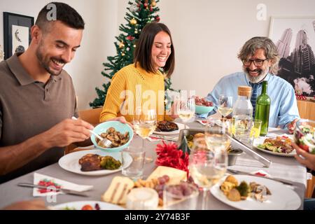 Lachende europäische, vielfältige Familie, die Spaß hat, Weihnachten zu Hause zu feiern und festlichen Esstisch zu sitzen Stockfoto