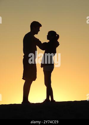 Eine Reihe von fesselnden Silhouetten, die ein Paar mit zarten Momenten bei Sonnenuntergang zeigt und eine ruhige und romantische Atmosphäre schafft. Stockfoto