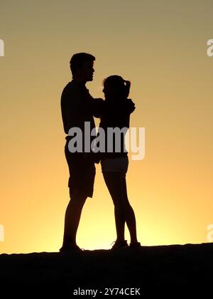 Eine Reihe von fesselnden Silhouetten, die ein Paar mit zarten Momenten bei Sonnenuntergang zeigt und eine ruhige und romantische Atmosphäre schafft. Stockfoto