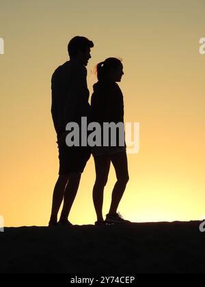 Eine Reihe von fesselnden Silhouetten, die ein Paar mit zarten Momenten bei Sonnenuntergang zeigt und eine ruhige und romantische Atmosphäre schafft. Stockfoto