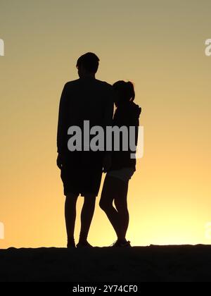 Eine Reihe von fesselnden Silhouetten, die ein Paar mit zarten Momenten bei Sonnenuntergang zeigt und eine ruhige und romantische Atmosphäre schafft. Stockfoto