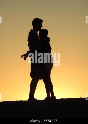 Eine Reihe von fesselnden Silhouetten, die ein Paar mit zarten Momenten bei Sonnenuntergang zeigt und eine ruhige und romantische Atmosphäre schafft. Stockfoto