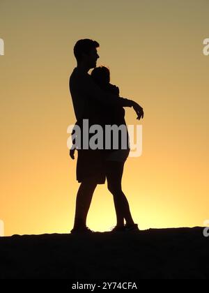 Eine Reihe von fesselnden Silhouetten, die ein Paar mit zarten Momenten bei Sonnenuntergang zeigt und eine ruhige und romantische Atmosphäre schafft. Stockfoto