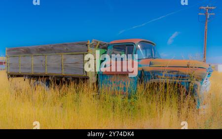 Ein alter verlassener Truck auf dem Feld mit hellen Farben und Holzlaster auf der Rückseite. Der Lkw ist umgeben von Gras und blauem Himmel mit Textraum. Stockfoto