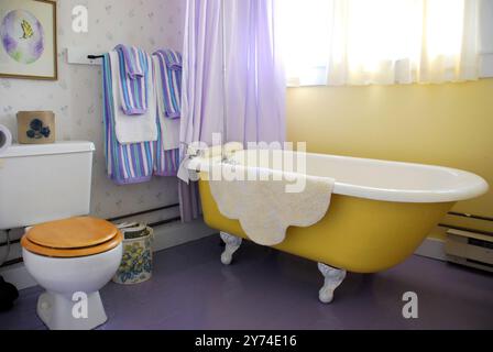 Foto: Helles Badezimmer mit gelber Badewanne mit Klauenfuß und blauen Vorhängen und Handtüchern Stockfoto