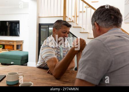 Armwrestling, zwei Seniorenfreunde, die am Tisch im Wohnzimmer antreten, zu Hause Stockfoto