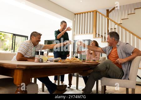Gemeinsam feiern Seniorenfreunde, die Drinks am Esstisch drinnen, zuhause, trinken Stockfoto