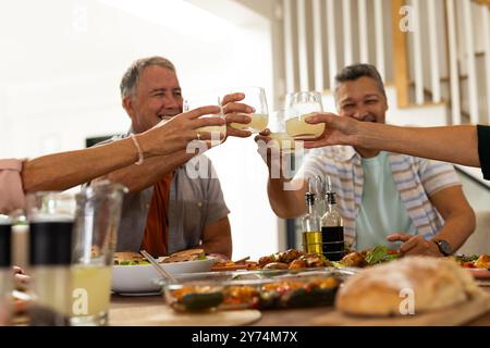 Bei Drinks toasten, verschiedene ältere Freunde, die gemeinsam am Esstisch essen, zu Hause Stockfoto