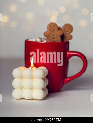 Brennende Kerze und heißes Getränk in roter Tasse mit Ingwerman-Keksen und Marshmallows. Heiße Schokolade oder Kakao. Weihnachtszeit. Stockfoto