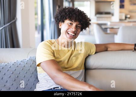 Lächelnder junger Mann, der sich auf dem Sofa in einem modernen Wohnzimmer entspannt und die Freizeit zu Hause genießt Stockfoto