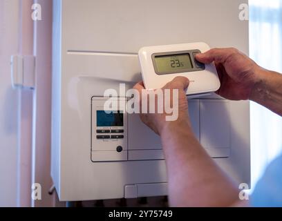 Eine Person, die die Temperaturregelung an einem drahtlosen Thermostat neben einem Heizkessel einstellt. Ein Konzept der Technologienutzung. Stockfoto