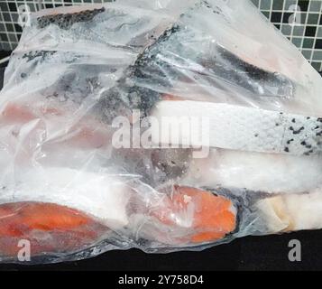 Sack mit gefrorenem rotem Fisch ist auf einer Theke. Die Lachse werden in Stücke geschnitten. Stockfoto