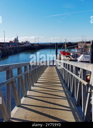 Blick auf den Fußweg der Arbroath Outer Harbour Pontons zu den Handelsschiffen, die neben Hochwasser vertäut sind. Stockfoto