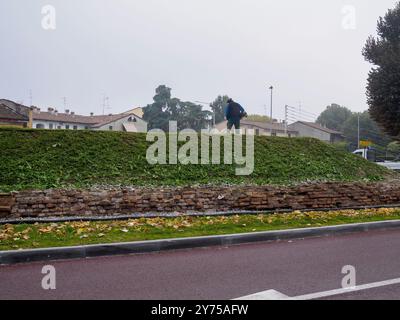 Cremona, Italien 26. September 2024 Ein Gärtner schneidet das Gras, das auf den antiken römischen Mauerruinen einer Stadt wächst Stockfoto