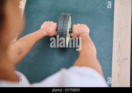 Eine fokussierte Person, die eine Übung mit einem ab-Roller auf einer Yoga-Matte durchführt und dabei die Stärke und Fitness des Kerns im Fitnessstudio betont. Stockfoto