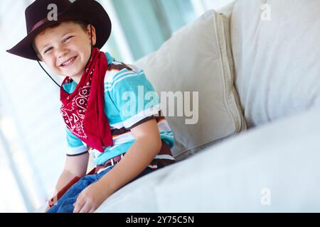 Cowboy, Kostüm und Porträt des Kindes auf Sofa mit Lächeln für Cosplay, Charakteroutfit und Cartoon. Glücklich, entspann dich und Junge mit Hut Stockfoto