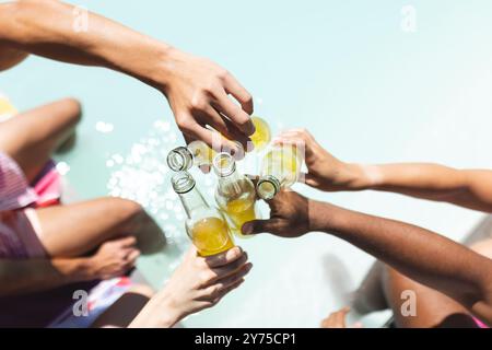 Mit Bierflaschen toasten, im Sommer treffen sich verschiedene Freunde am Pool, zu Hause Stockfoto