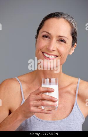 Glückliche Frau, Porträt und Milch mit Glas für Kalzium, Diät oder Getränk im Studio auf grauem Hintergrund. Reife, weibliche Person oder Model mit Lächeln oder Stockfoto