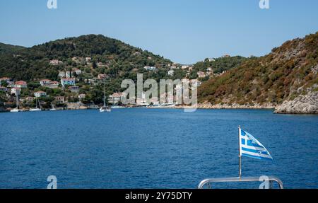 Griechische Flagge winkt auf dem Boot und nähert sich dem malerischen Dorf in griechenland Stockfoto