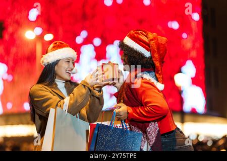 Zwei glückliche Frauen tauschen nachts im Freien weihnachtsgeschenke aus Stockfoto